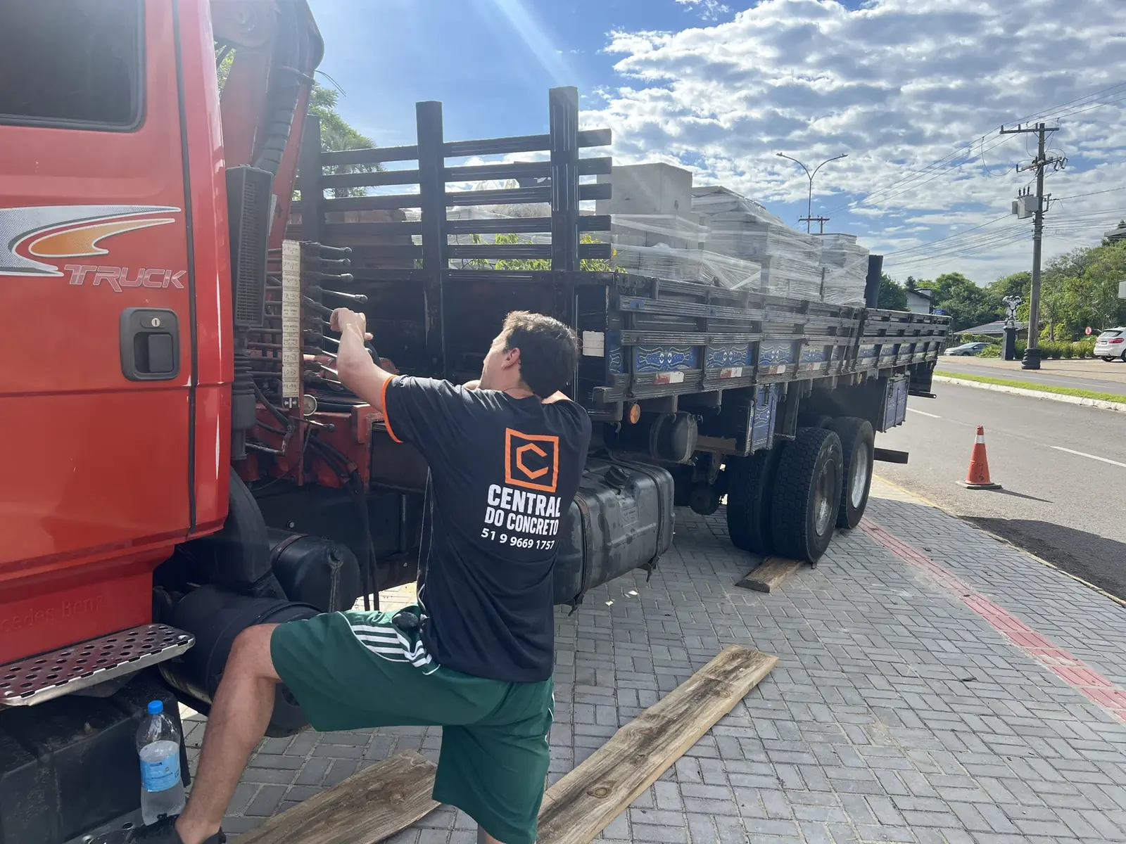 Funcionário em camiseta da Central do Concreto opera descarga em caminhão truck Mercedes carregado com pré-moldados embalados em stretch · operação real de entrega no raio de 120 km · Central do Concreto Ivoti RS