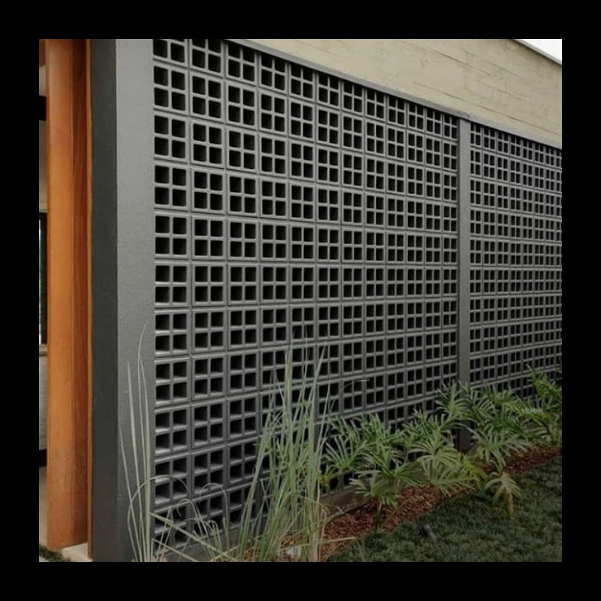 Muro alto construído com cobogós Ao Quadrado em concreto pré-moldado pintados em tom grafite escuro, padrão de pequenos quadrados vazados em malha densa, ambiente residencial externo com jardim · Central do Concreto Ivoti RS