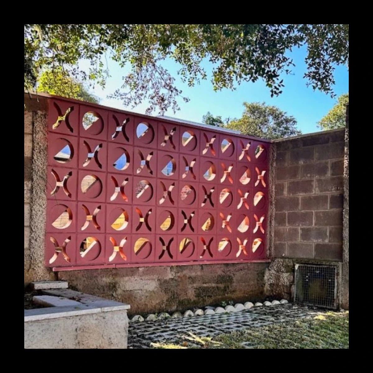 Muro construído com cobogós Fenestra em concreto pré-moldado pintados em tom bordô vermelho, padrão de arcos duplos formando textura visual orgânica, ambiente externo com vegetação · Central do Concreto Ivoti RS