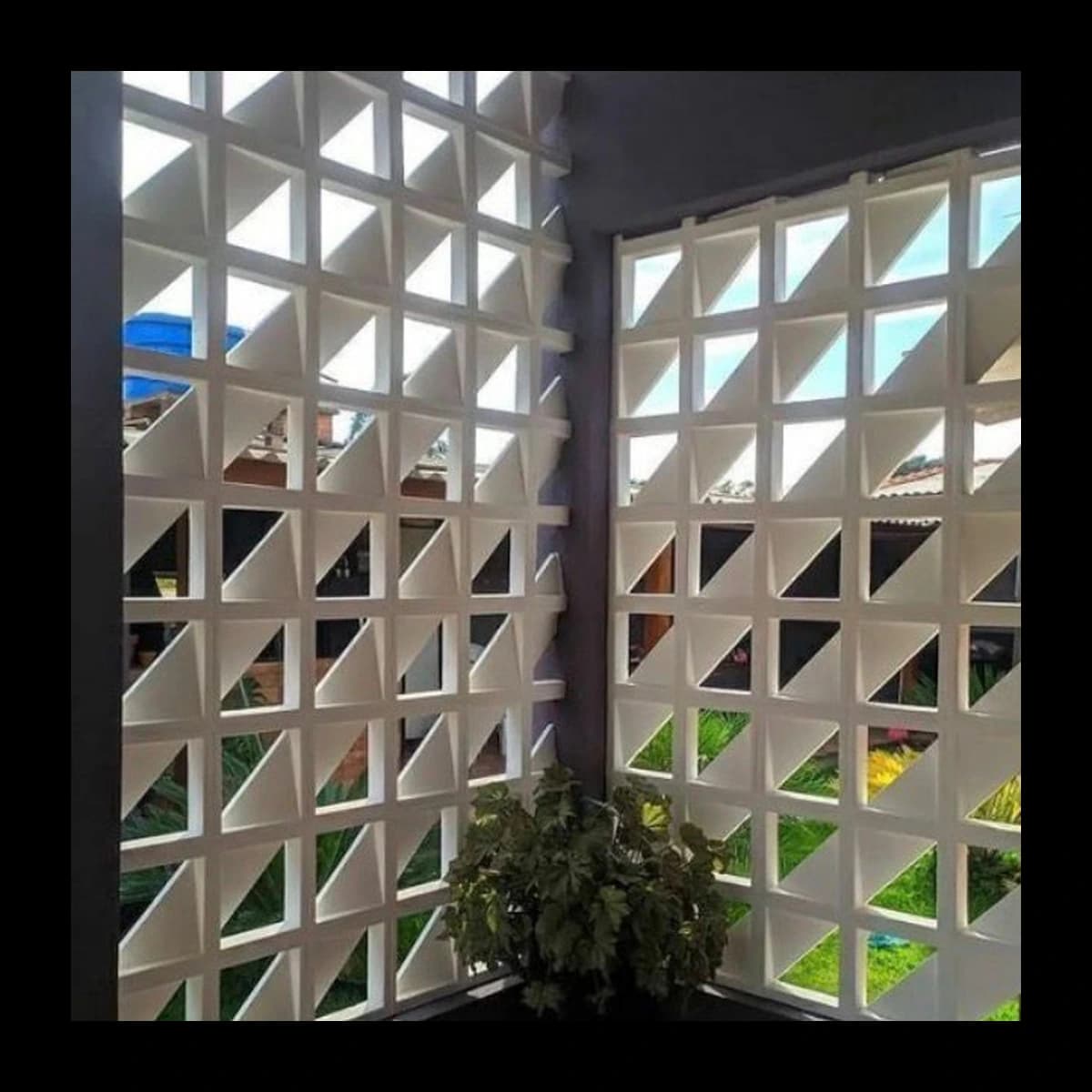 Muro de canto duplo construído com cobogós Urbano em concreto pré-moldado, módulos quadrados subdivididos por diagonal com vazado triangular, ambiente externo com vegetação · Central do Concreto Ivoti RS