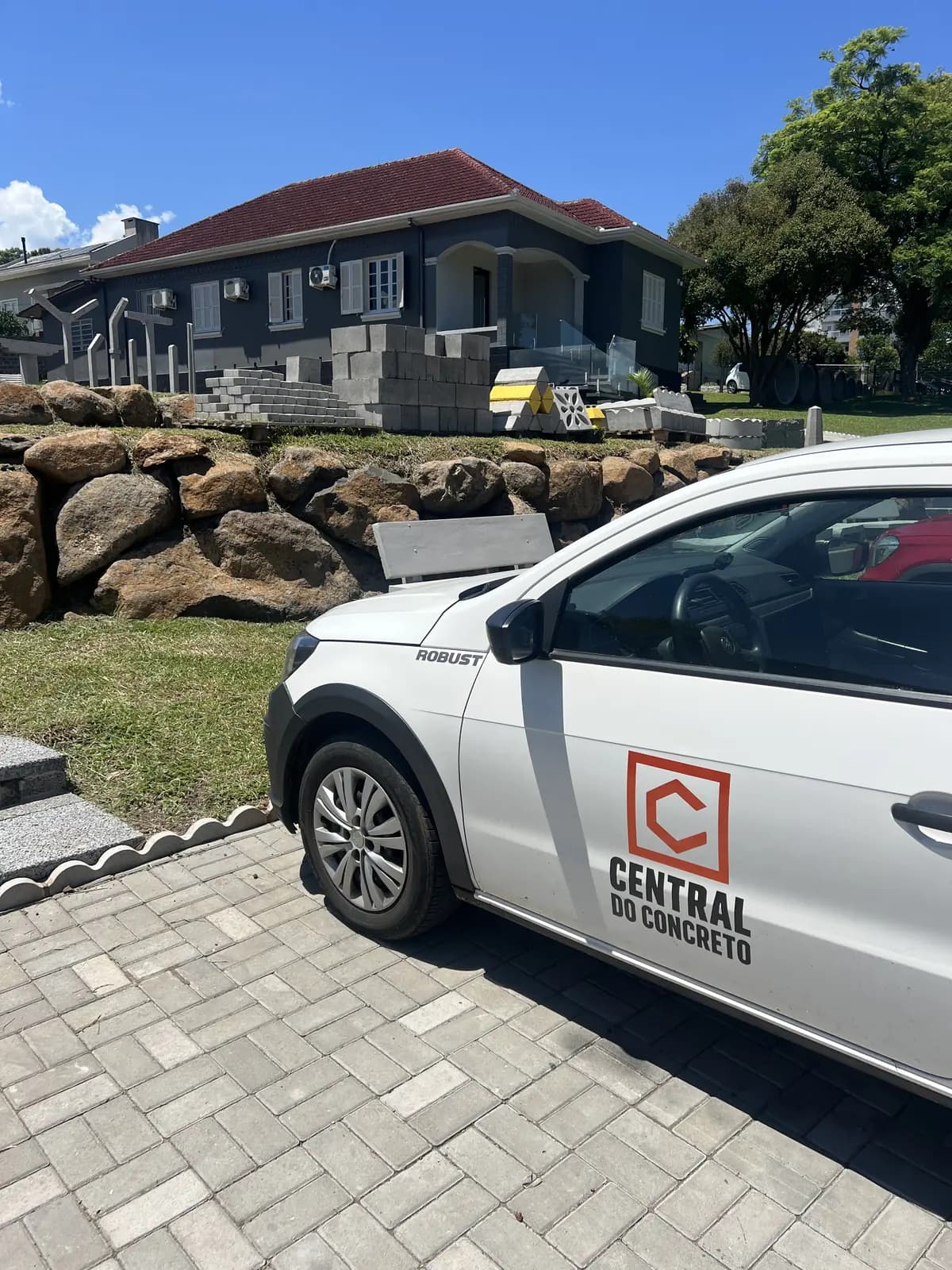 Veículo Saveiro branca da Central do Concreto estacionada em pavimento de paver na sede operacional em Ivoti com estoque de cobogós empilhados ao fundo · entrega no raio de 120 km com caminhão próprio · Central do Concreto Ivoti RS