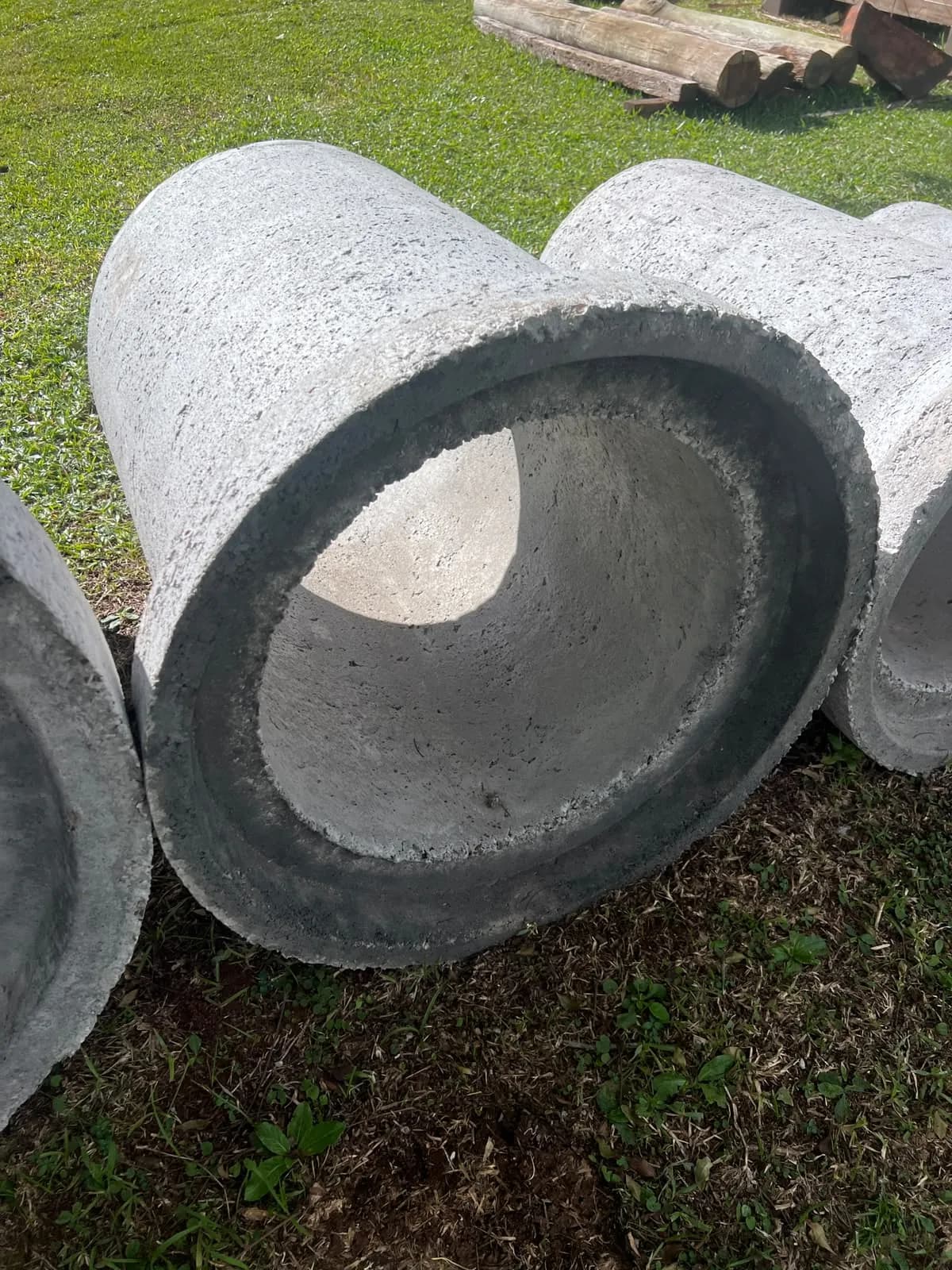 Tubo de concreto deitado na grama, visto pela boca, com a parede e o interior à mostra