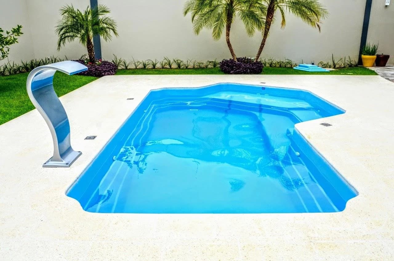 Piso atérmico ao redor de uma piscina, com uma cascata ao lado e palmeiras ao fundo