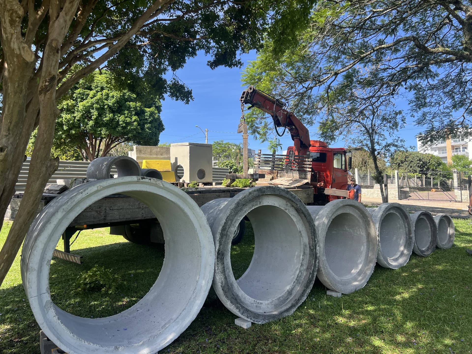 Tubos de concreto armado em fila com caminhão munck vermelho ao fundo, pátio da Central do Concreto em Ivoti durante operação diurna.